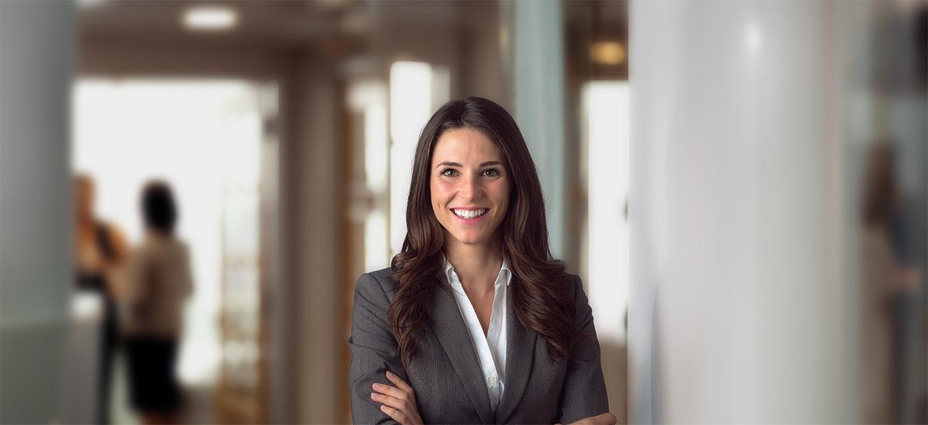 Confident businesswoman smiling with arms crossed in a professional office hallway.