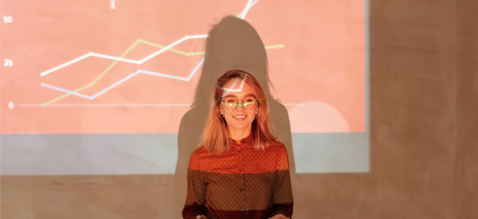 Smiling woman standing in front of a projected graph during a presentation.