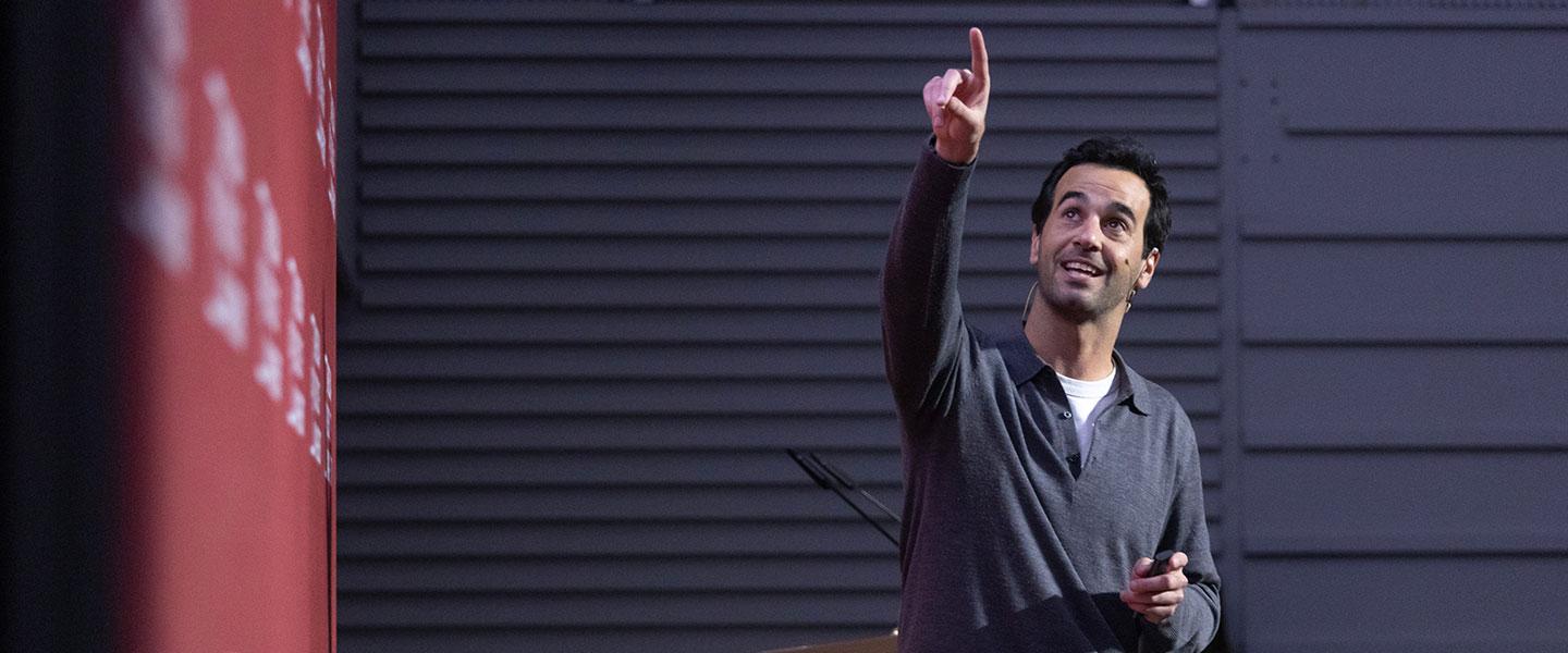 Speaker presenting on stage and pointing to a screen during a talk or conference at an academic event